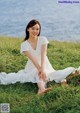 A woman in a white dress sitting on the grass by the water.